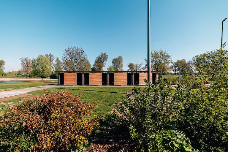 Blick auf die Liegewiese und einige Umkleiden, die mit Holz verkleidet sind.