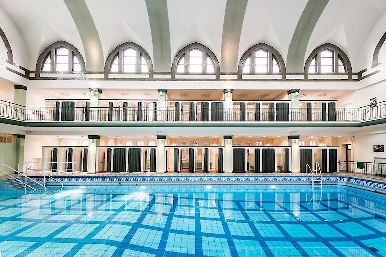 Schwimmhalle mit basilikale Gewölbe. Mehrzweckbecken sowie die Umkleiden, die auf zwei Etagen um das Becken herum verteilt sind.