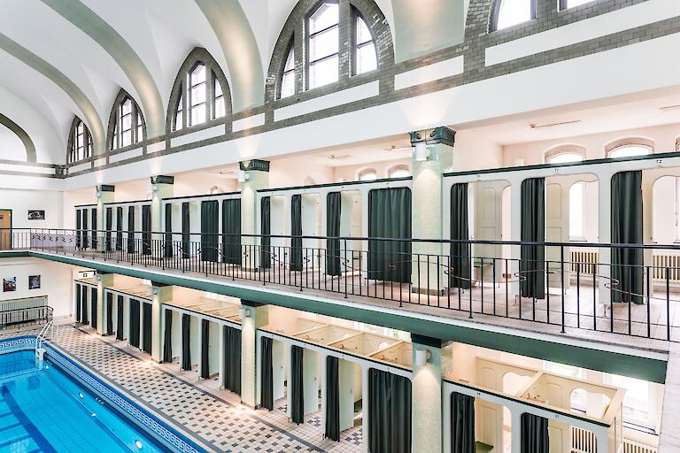 Schwimmhalle mit basilikale Gewölbe. Die Umkleiden sind auf zwei Etagen um das Becken herum verteilt.