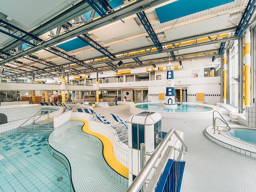 Schwimmhalle im Freizeitbad Düsselstrand. Das Bewegungsbecken hat einen Leuchtturm in der Beckenmitte, das Spiel- und Tummelbecken mit einer Reifenrutsche sowie ein Whirlpool.