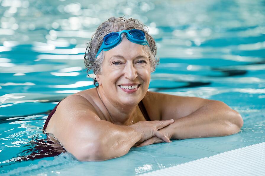 Glückliche Seniorin ist im Wasser und legt Ihre Arme auf den Beckenrand.