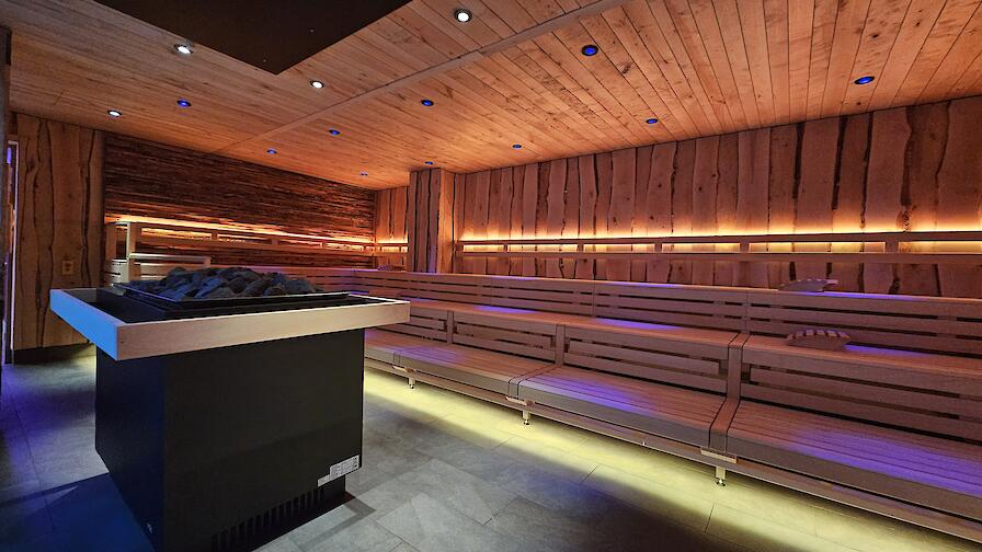 Beleuchtete Aufguss-Sauna „Löyly“ mit einem Saunaofen in der Mitte.