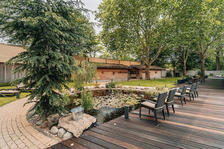 Saunagarten mit Teich, Stühlen auf der Terrasse und im Hintergrund zwei Saunen.