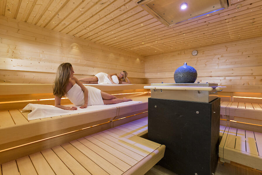 Meer-Sauna mit einem Sternenhimmel und einer großen Granitkugel auf dem Saunaofen. Zwei Frauen liegen in der Sauna.