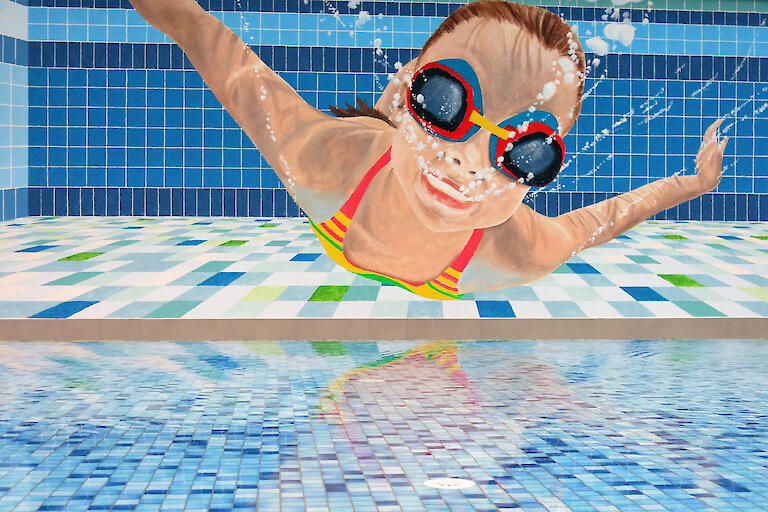 Wandbild in der Schwimmhalle von einem Mädchen, welches gerade unter Wasser taucht.