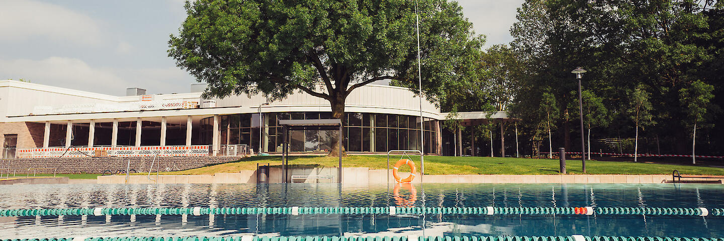 Der Bereich des Mehrzweckbeckens, in dem Leinen gespannt sind um das Schwimmen auf 50m-Bahnen zu ermöglichen. Im Hintergrund das Gebäude des Hallenbades.