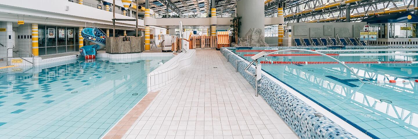 Schwimmhalle im Freizeitbad Düsselstrand. Übungsbecken mit Wasserballtor, Wasser-Basketballkorb und Kinder-Schlangenrutsche sowie ein Ende des 25m-Beckens.