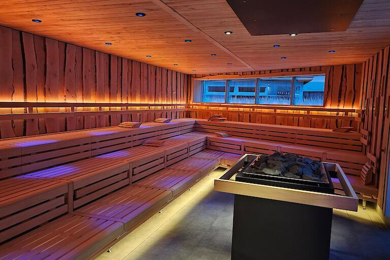 Beleuchtete Aufguss-Sauna „Löyly“ mit einem Saunaofen in der Mitte und Fenstern in den Saunagarten.