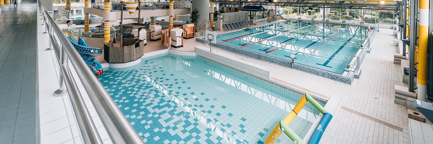 Schwimmhalle im Freizeitbad Düsselstrand. Übungsbecken mit Wasserballtor, Wasser-Basketballkorb und Kinder-Schlangenrutsche sowie das 25m-Beckens mit fünf Bahnen davon eine Schwimmerautobahn sowie Startblöcken.