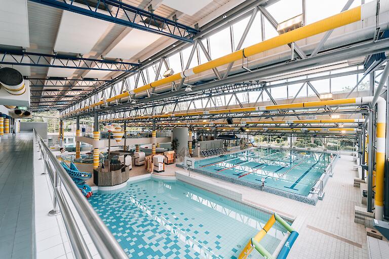 Schwimmhalle im Freizeitbad Düsselstrand. Übungsbecken mit Wasserballtor, Wasser-Basketballkorb und Kinder-Schlangenrutsche sowie das 25m-Beckens mit fünf Bahnen davon eine Schwimmerautobahn sowie Startblöcken.