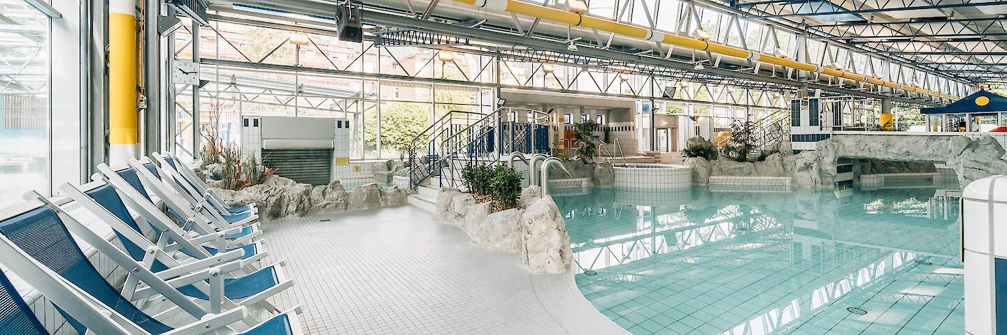 Schwimmhalle im Freizeitbad Düsselstrand. Das Spiel- und Tummelbecken mit einer Reifenrutsche und blaue Liegestühle stehen am Beckenrand.