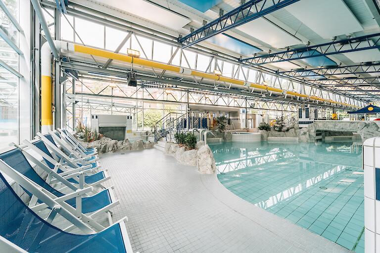 Schwimmhalle im Freizeitbad Düsselstrand. Das Spiel- und Tummelbecken mit einer Reifenrutsche und blaue Liegestühle stehen am Beckenrand.
