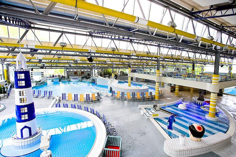 Schwimmhalle im Freizeitbad Düsselstrand. Das Bewegungsbecken hat einen Leuchtturm in der Beckenmitte, das Spiel- und Tummelbecken mit einer Reifenrutsche sowie das Kleinkind-Planschbecken mit einer kleinen Rutsche.