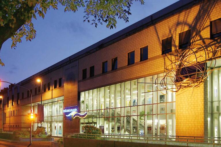 Außenansicht im Dunkeln des Freizeitbades Düsselstrand mit einer großen Glasfront zur Straße hin.