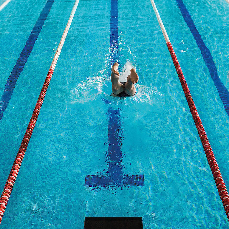drei Bahnen im Schwimmbad mit drei Menschen die jeweils auf einer Bahn schwimmen.