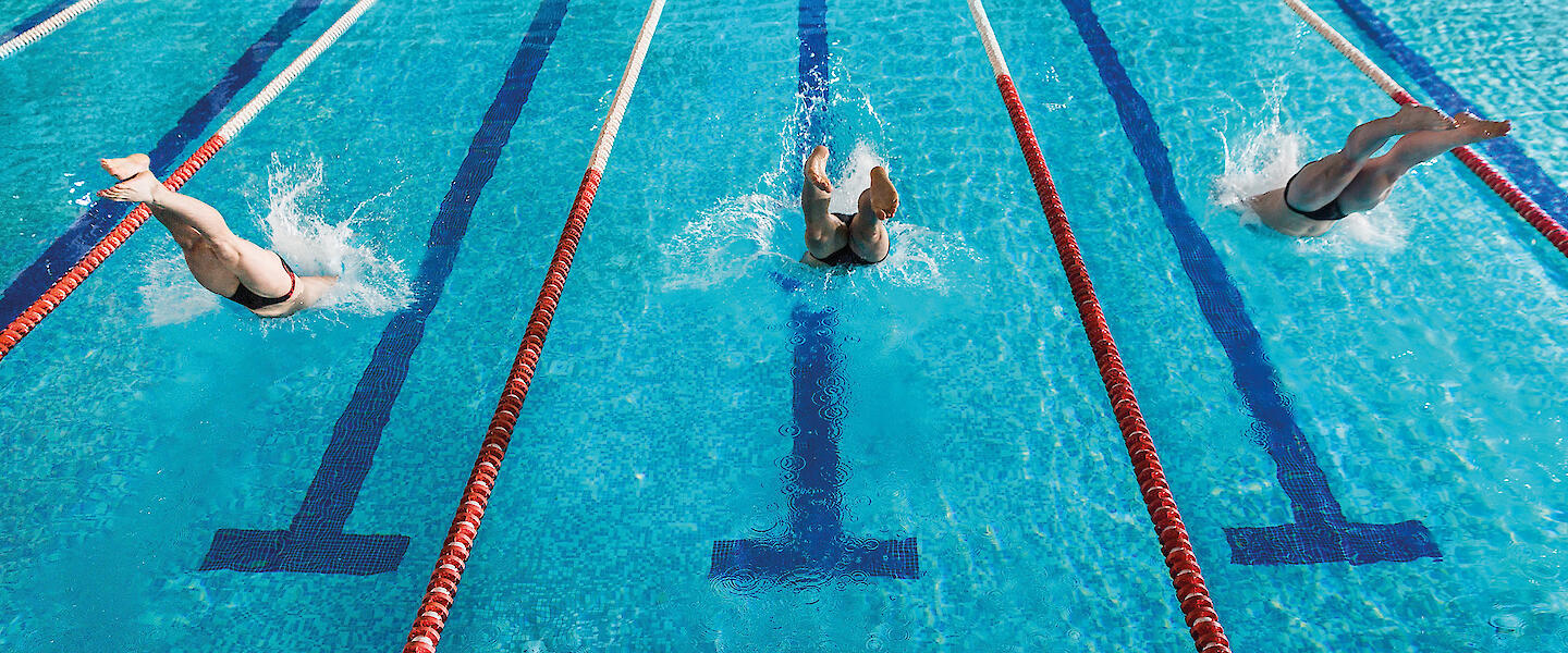 drei Bahnen im Schwimmbad mit drei Menschen die jeweils auf einer Bahn schwimmen.